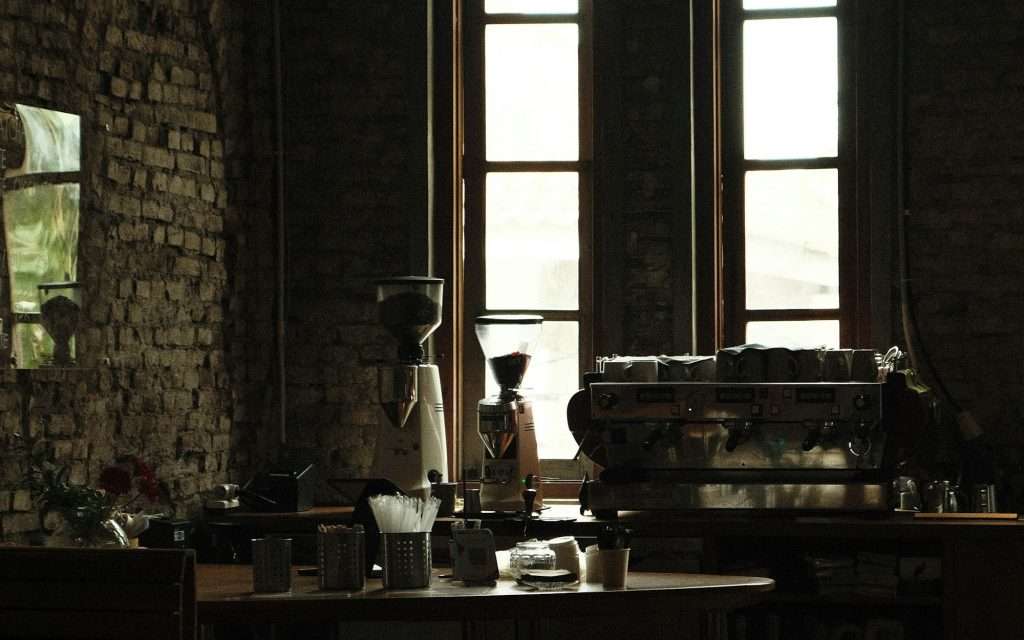 Cafédisk med två kaffekvarnar och en espressomaskin framför höga fönster