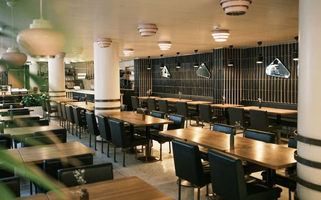 Tom restaurangmatsal med träbord, mörkgröna stolar och pendellampor